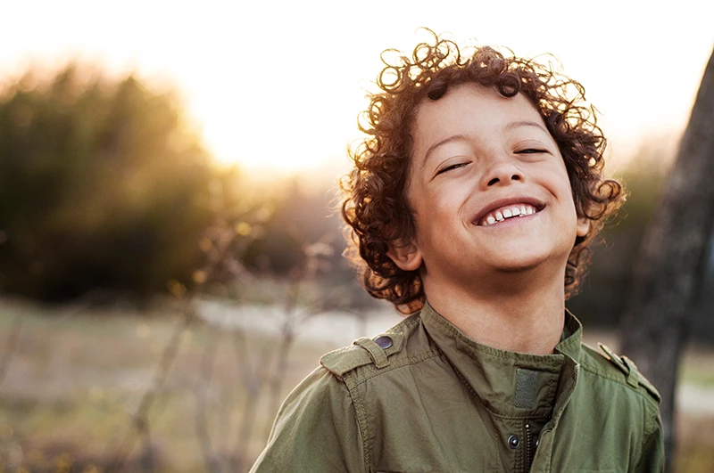 a little boy smiling outside in a meadow