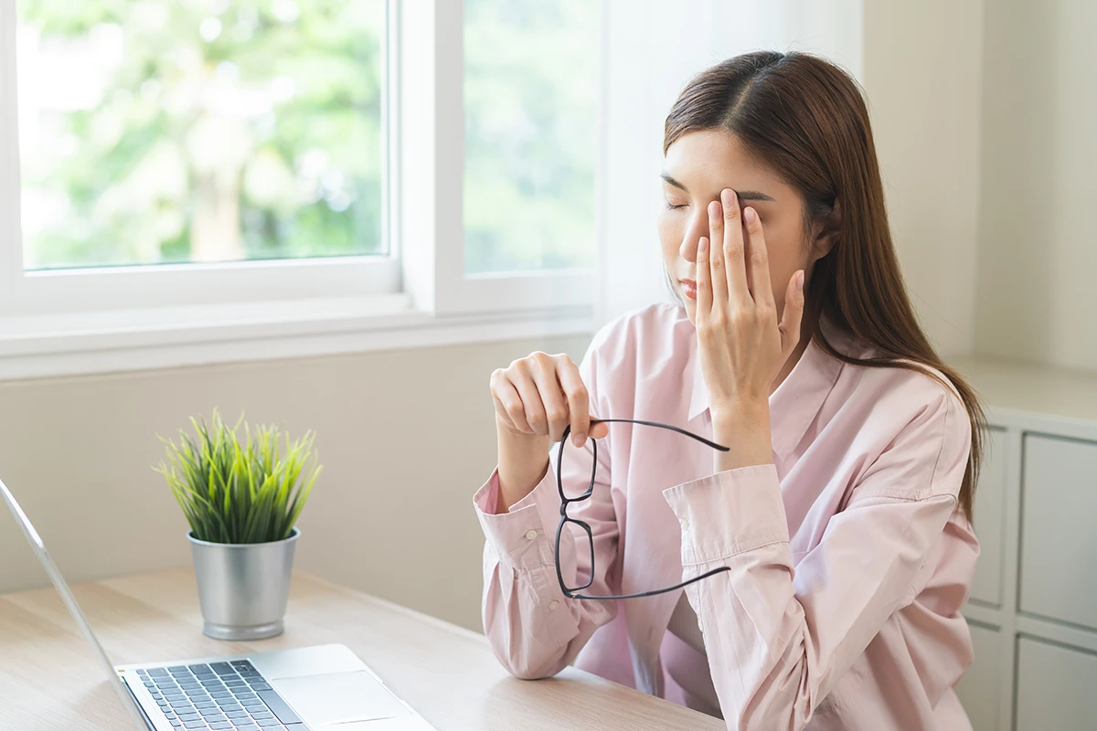 a woman at home taking off her glasses and holding a hand to her eye